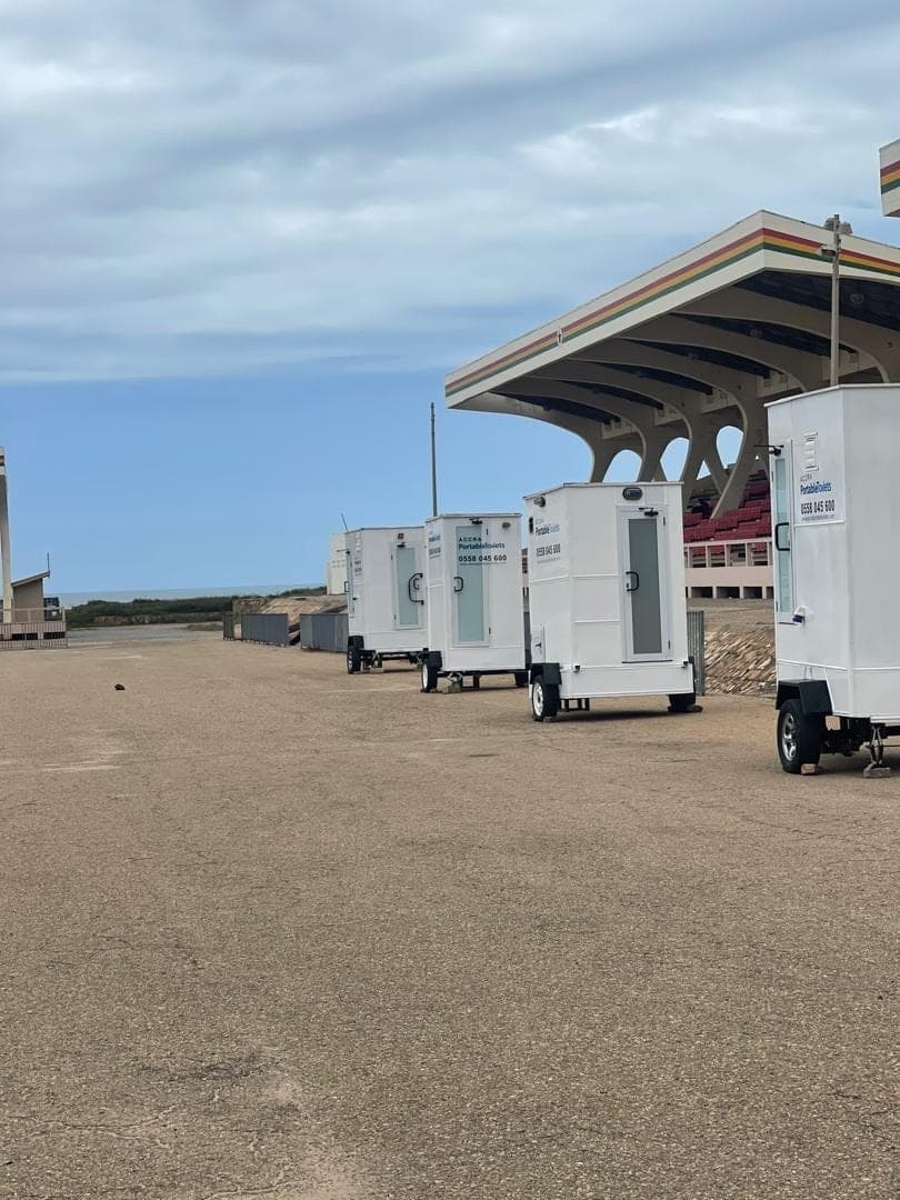 A row of restroom trailers lined up on tarmac beside an event pavilion