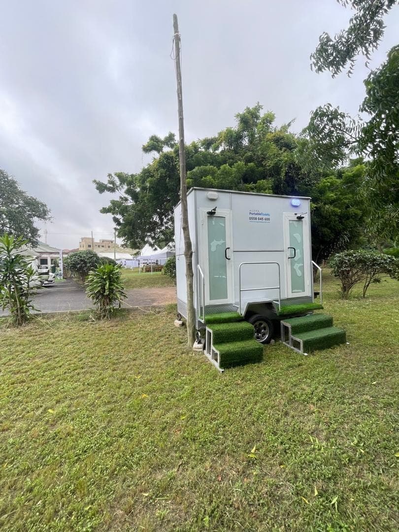 Restroom trailer standing on open grass under a cloudy sky
