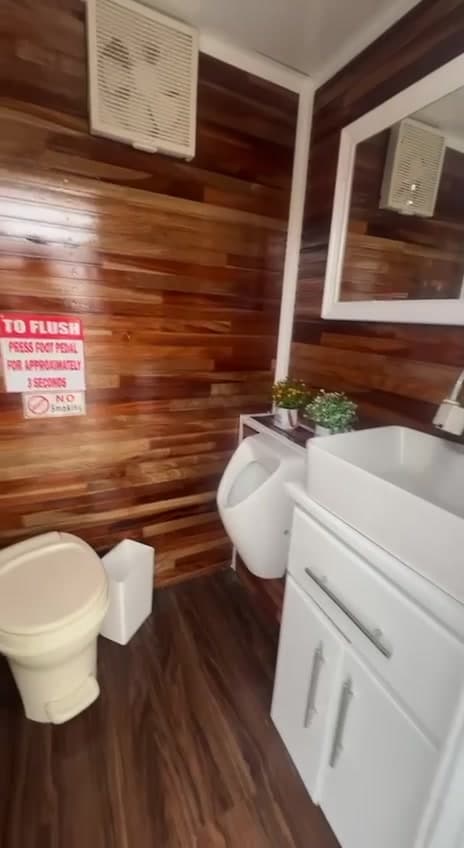 Inside a restroom trailer — timber-clad walls, ceramic WC, urinal and vanity basin